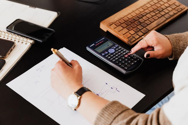 Accueil crop woman using calculator and taking notes on paper